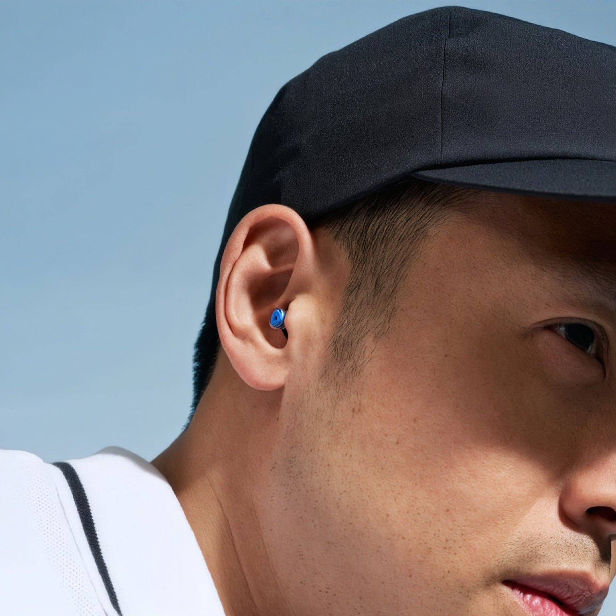 Alpine 24h Le Mans® earplug worn in the ear by a man in a black cap and white shirt