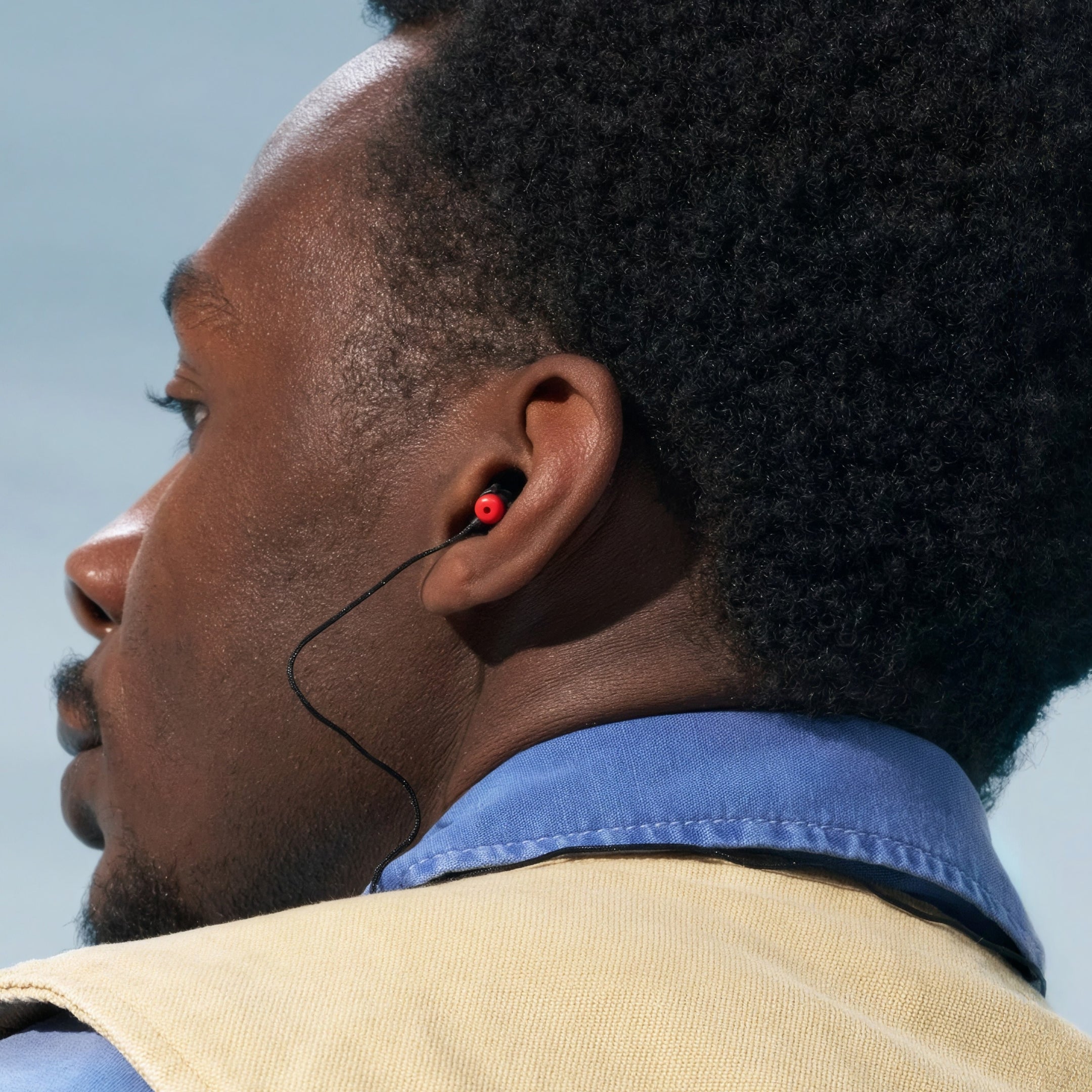 Man in a blue shirt and beige vest wearing Alpine WorkSafe earplugs with a cord, side view